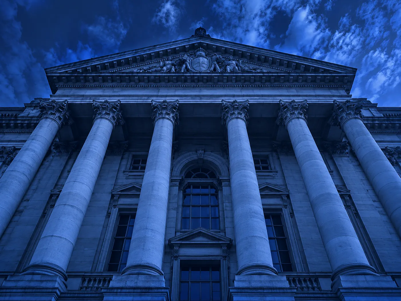Stylised low-angle view of a neoclassical civic building facade with tall columns against a deep blue sky.